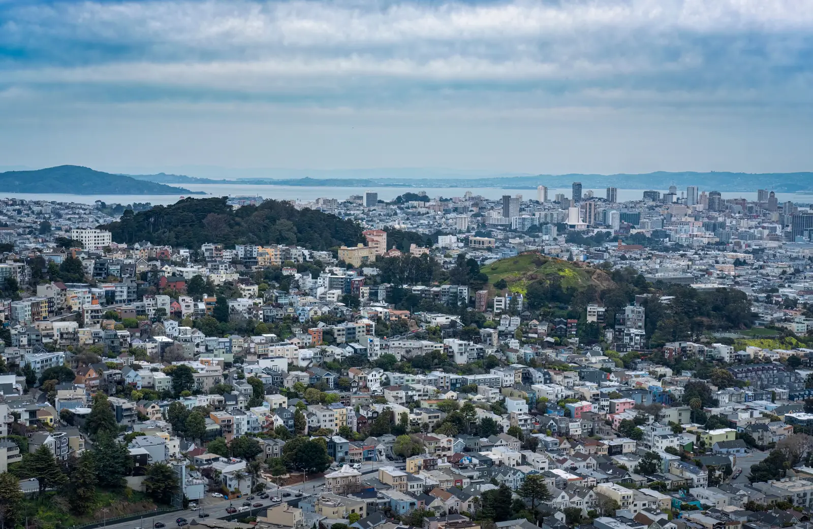 A city seen from above, residential streets climbing the hills in the foreground and the downtown skyline meeting the water in the distance
