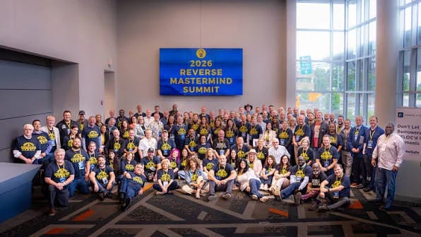 A large group of reverse mortgage professionals gathered for a photograph at an industry summit, in front of a screen reading 2026 Reverse Mastermind Summit